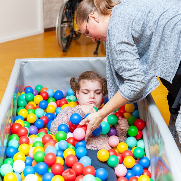 A young girl with an intellectual disability in a bin of therapy balls at a physiotherapy session