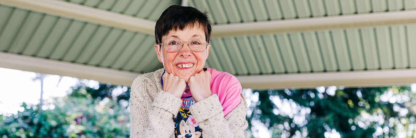Individual with glasses resting her chin on her fists in an outdoor gazebo setting