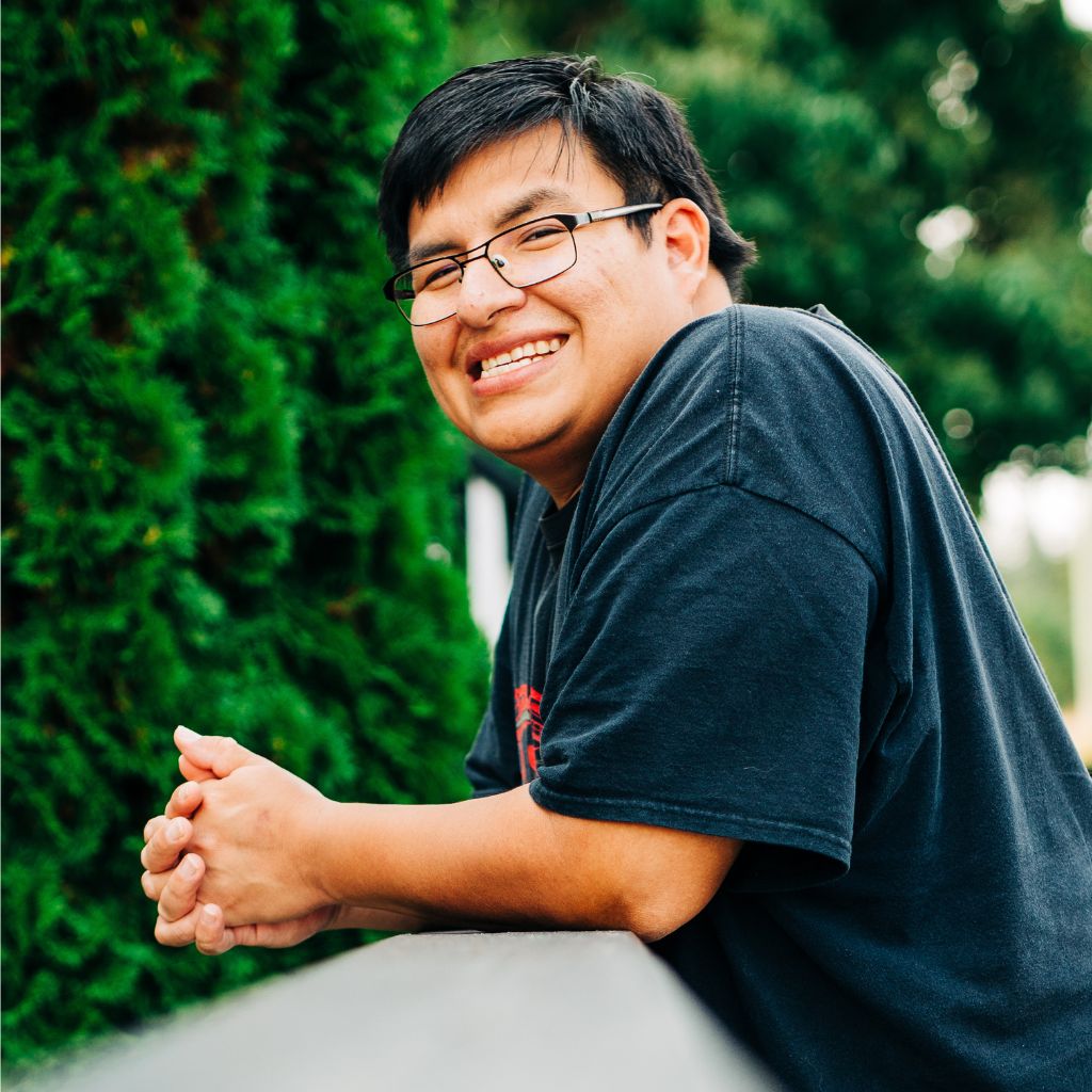 A young man with an intellectual disability leaning on a railing and smiling at the camera