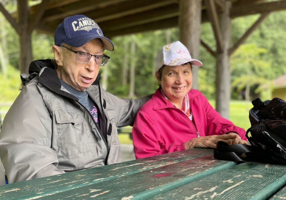 Image of two individuals sitting at a picnic table posing for the camera. 