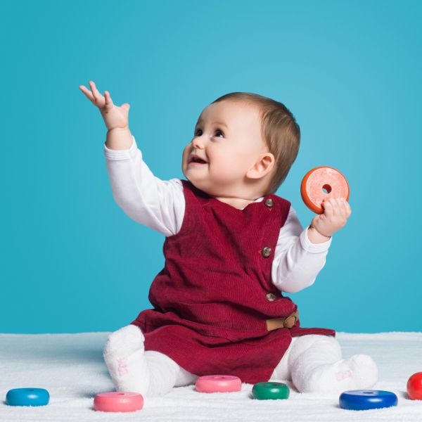 A baby in a red dress playing with plastic rings