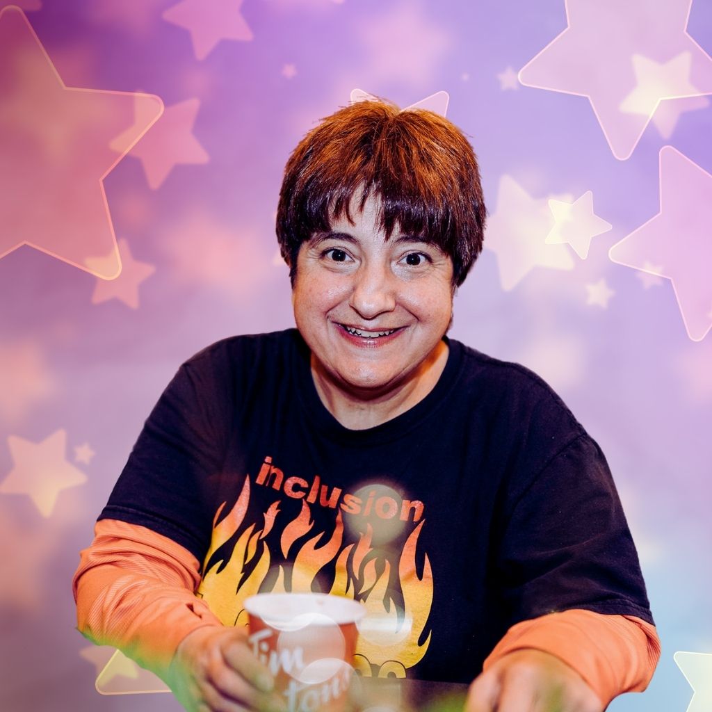 An individual with an intellectual disability holding a coffee and wearing a flame shirt with the word inclusion on it