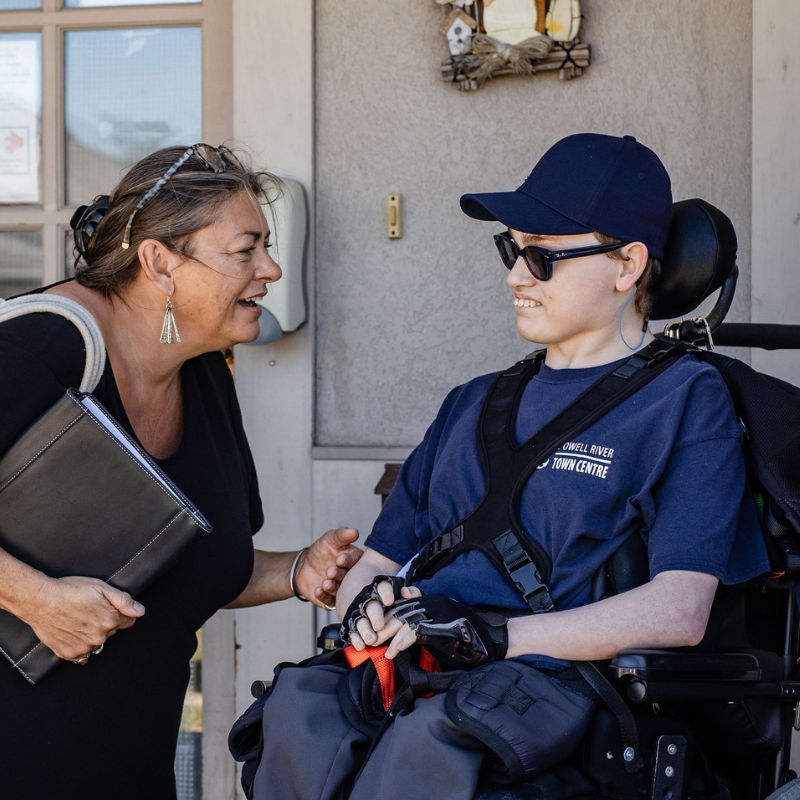 An inclusion employee bent down speaking with a young man with an intellectual disability in a wheelchair