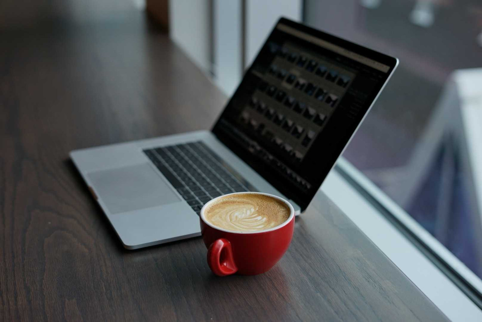 A laptop and coffee mug on a desk in front of a window