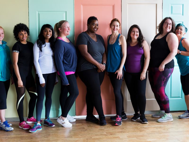 A group of diverse women wearing athletic gear standing in front of colorful lockers - inclusion powell river